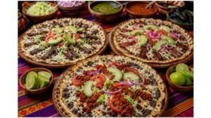 Close-up of a crispy Oaxacan tlayuda topped with tasajo, Oaxaca cheese, avocado, salsa, cilantro, and fresh vegetables.