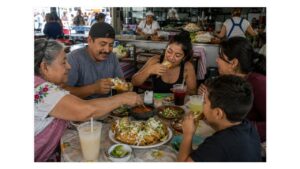 Mexican family sharing tacos dorados with salsa, crema, cheese, lime, and aguas frescas at a busy traditional market fonda.