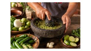 Fresh serrano peppers and tomatillos being ground in a traditional molcajete to make Mexican salsa verde.
